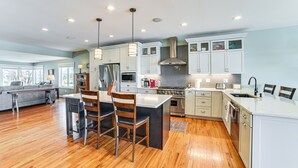A modern kitchen with wooden flooring, white cabinets, stainless steel appliances, and pendant lighting.