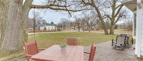 A patio with a wooden table and chairs, a potted plant, and a view of a house and trees.
