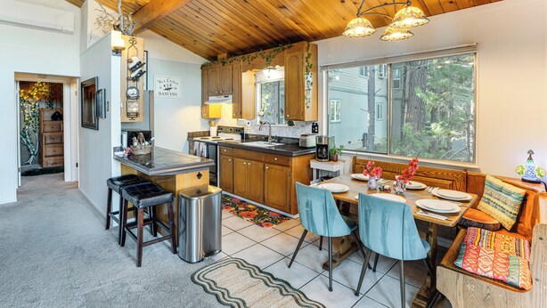 A cozy kitchen with wooden cabinets, a dining area with a bench, and a large window providing a view of the outdoors. - Enchanted Woodland Cabin Near Yosemite w/ Fire Pit (Groveland)