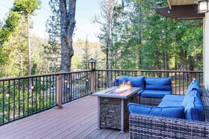 A deck with outdoor furniture and a fire feature, surrounded by trees.