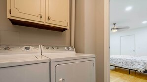 A laundry area with a washer and dryer, a bed with a floral bedspread, and a ceiling fan. - Pool & Game Room: Spacious Brandon Home (Brandon)
