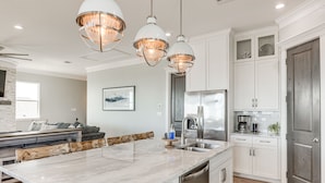 Une cuisine moderne avec des meubles blancs, un îlot en marbre, des appareils en acier inoxydable et des luminaires suspendus.
