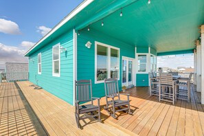 A turquoise building with a wooden deck, two rocking chairs, and a table. - Luxe Freeport Home: Steps to the Sand! (Freeport)