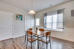 A dining area with a wooden table and chairs, white doors, a window with blinds, and a hanging light fixture.