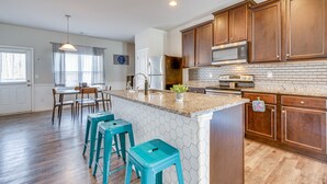 A kitchen with wooden cabinets, a granite countertop, and a stainless steel refrigerator. There are four turquoise stools and a dining table with chairs. - Union City Townhome: 17 Mi to Downtown Atlanta! (Union City)