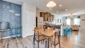 A modern kitchen with a brick backsplash, stainless steel appliances, and a wooden dining table with chairs. - Union City Townhome: 17 Mi to Downtown Atlanta! (Union City)