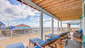 Un terrazzo in legno con poltrona relax e tavolo, con vista su una spiaggia e un molo di legno, con una casa sullo sfondo.