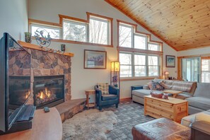 A cozy living room with a stone fireplace, wooden ceiling, and large windows. - Lakefront Tomahawk Getaway w/ Deck & 2 Fireplaces! (Tomahawk)