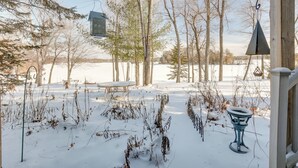 Eine verschneite Outdoor-Fläche mit einer Holzterrasse, einem hängenden Vogelhaus und einem Tisch.