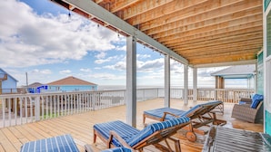 A wooden deck with lounge chairs and a table, overlooking a beach with a wooden pier and a house in the background. - 'footprints in the Sand' - Luxe Freeport Home! (Freeport)