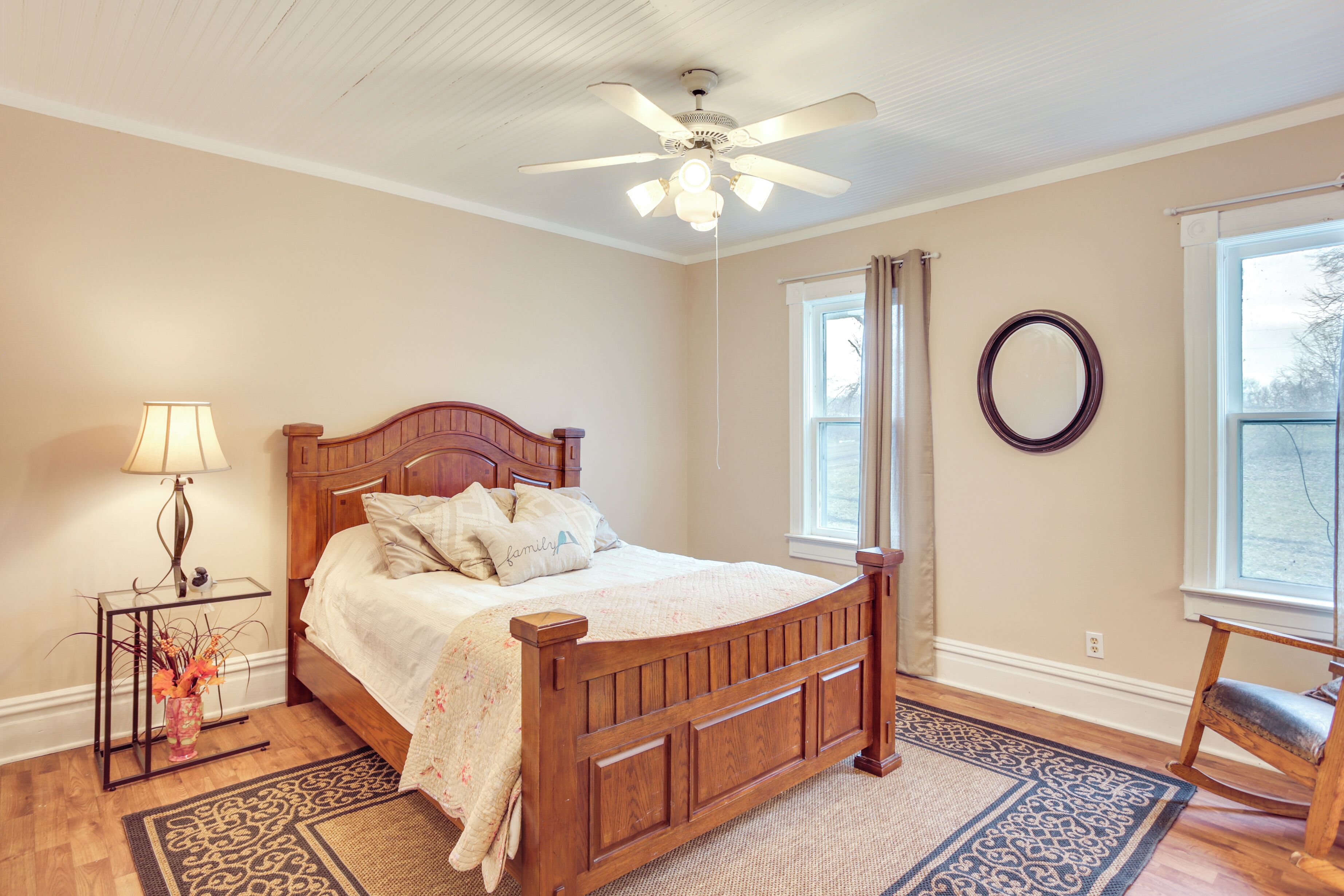 Une chambre à coucher avec un lit en bois, une table de chevet avec une lampe, un fauteuil à bascule et un ventilateur de plafond.