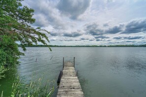 Een houten steiger die zich uitstrekt over een kalm meer, omringd door groen, onder een bewolkte lucht.