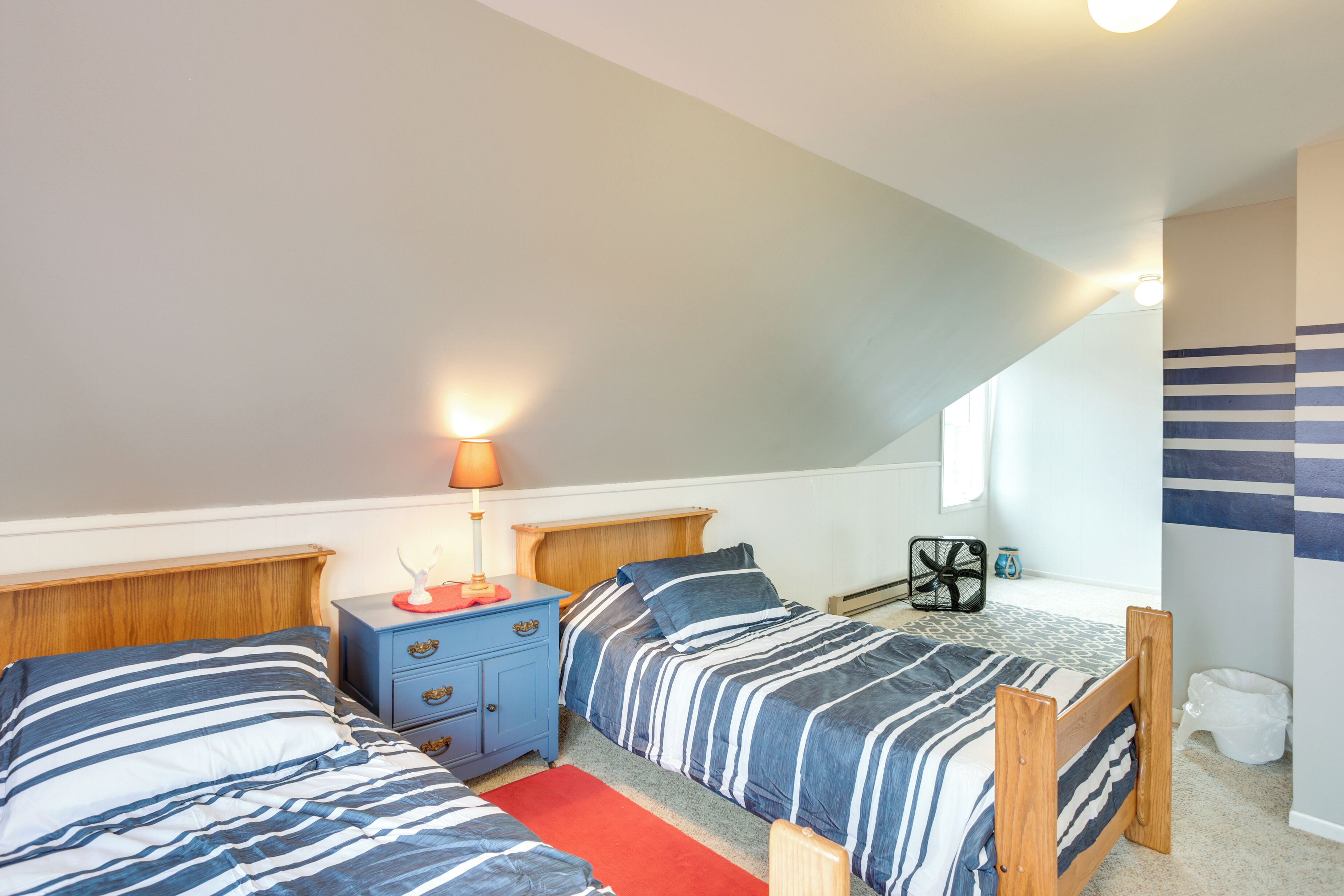 A bedroom with two beds, a nightstand, a lamp, and a fan.