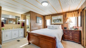 A bedroom with a wooden bed, a nightstand, a dresser, a mirror, and a bathroom with a vanity and sink. - Classic Country Retreat in Ronda on 5 Acres! (Ronda)