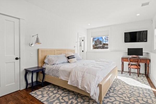 A bedroom with a bed, bedside table, lamp, TV, and a window with a view of a building.