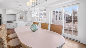 A modern kitchen with white cabinets, a central island, and a dining area with wicker chairs. - Stroll to Chatham's Popular Shops & Dining / Or Walk to Andrew Hardings Beach from This NEW Impeccable Compound (Chatham)