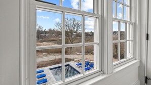 A large window with multiple panes overlooking a backyard with a swimming pool and lounge chairs. - Stroll to Chatham's Popular Shops & Dining / Or Walk to Andrew Hardings Beach from This NEW Impeccable Compound (Chatham)