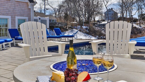 A poolside setting with a table set for a meal, including a bottle of wine, glasses, cheese, and grapes. - Stroll to Chatham's Popular Shops & Dining / Or Walk to Andrew Hardings Beach from This NEW Impeccable Compound (Chatham)
