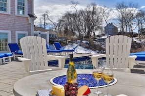 A poolside setting with a table set for a meal, including a bottle of wine, glasses, cheese, and grapes.