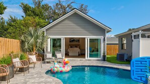 Un patio trasero con piscina, cercado de madera y mobiliario exterior.