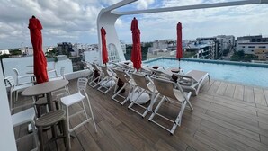 Un espace piscine aménagé sur le toit, avec des chaises longues et des parasols, offrant une vue sur le paysage urbain.