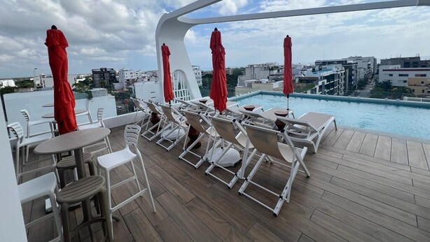 A rooftop pool area with lounge chairs and umbrellas, overlooking a cityscape. - Alizee Tower (Playa del Carmen)