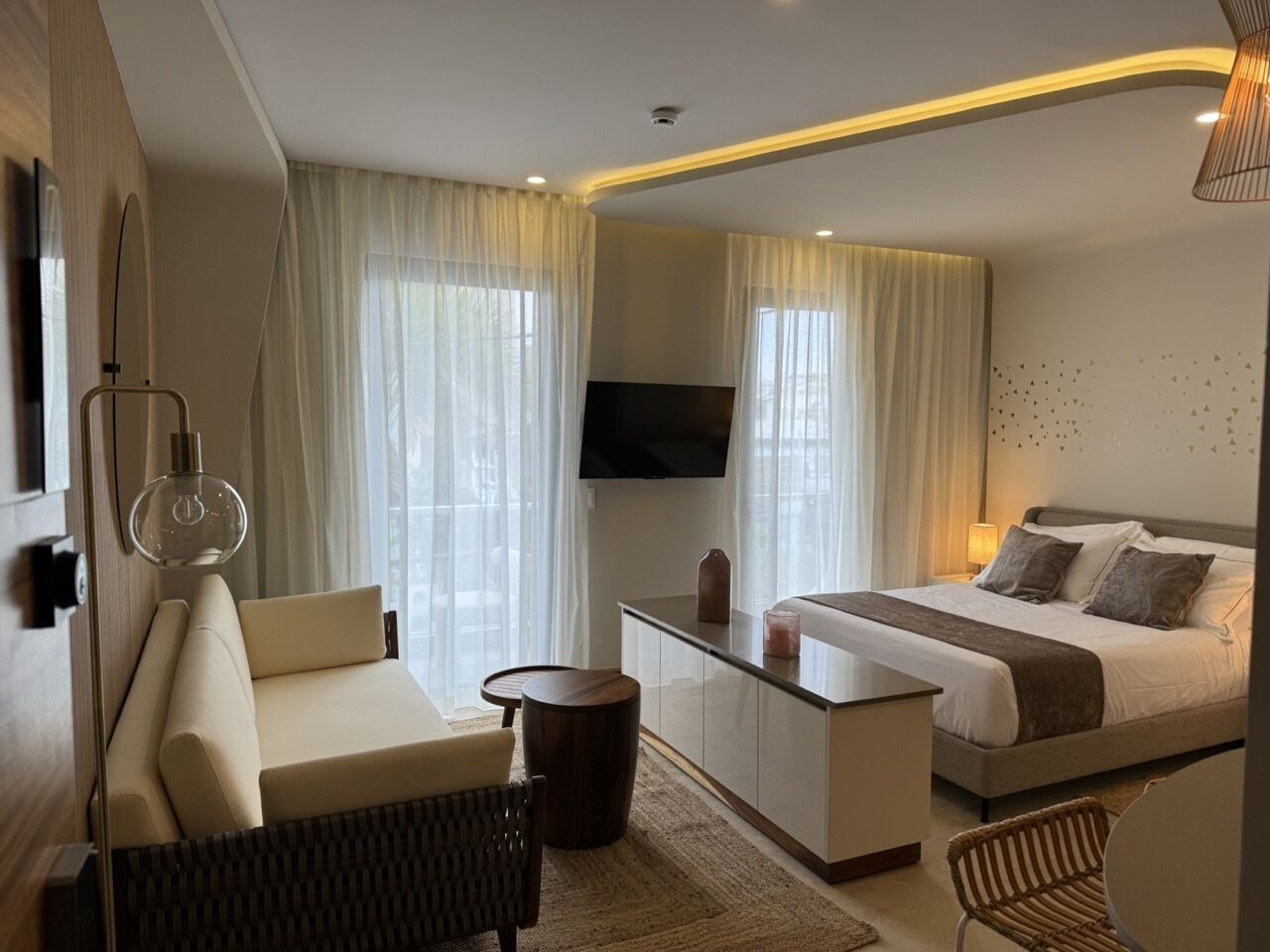 Ein modernes Hotelzimmer mit einer Couch, einem Bett, einem Fernseher und einer Glastrennwand.