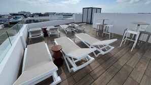 A rooftop terrace with white lounge chairs, a table, and a glass balustrade overlooking a cityscape. - Alizee Tower (Playa del Carmen)