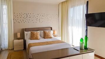 A modern hotel room with a large bed, bedside tables, a flat-screen TV, and a small seating area.