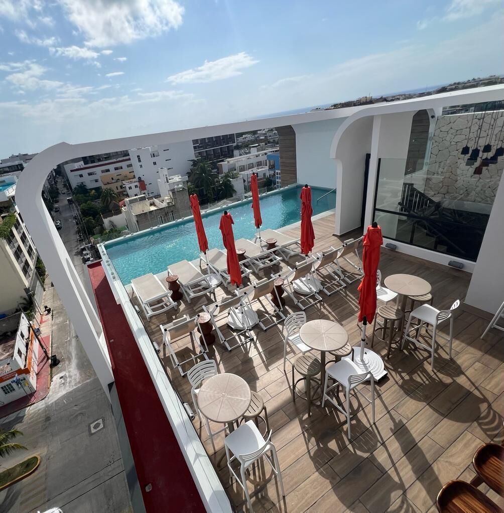 Un espace piscine aménagé sur le toit, avec des chaises longues et des parasols, offrant une vue sur le paysage urbain.