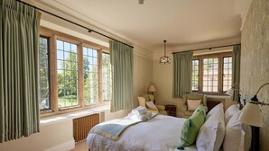 A bedroom with a large bed, two windows with curtains, a radiator, a lamp, and a chair. - Rhodes House (Oxford)