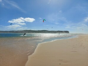 Una playa con cielos despejados, personas practicando windsurf y cometas volando.