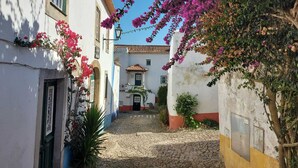 A narrow cobblestone street flanked by white buildings with red and blue trim, leading to a building with a tiled roof. - Spacious 4 bed house with hot tub, games room & terraces, near Alcobaca & Nazare (Vestiaria)