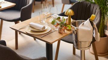 Un restaurante con mesas dispuestas para comer, sillas, una planta en maceta y una botella de champán sobre una mesa.