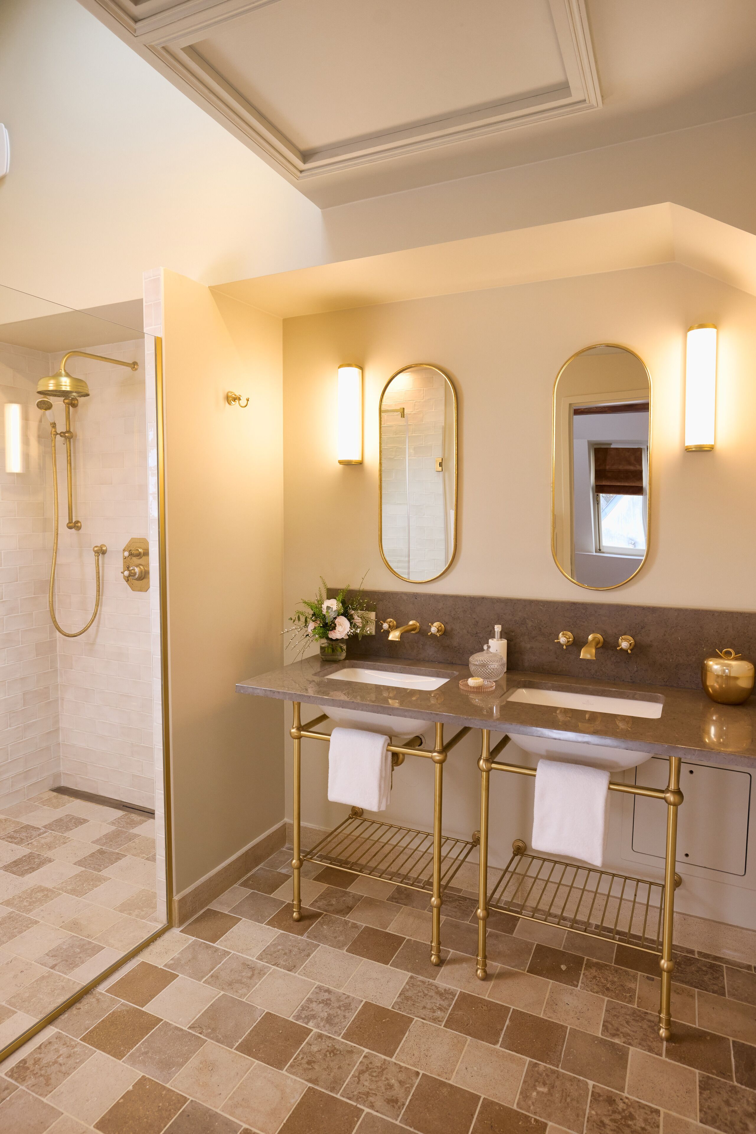 A bathroom with two sinks, a shower, and gold fixtures.