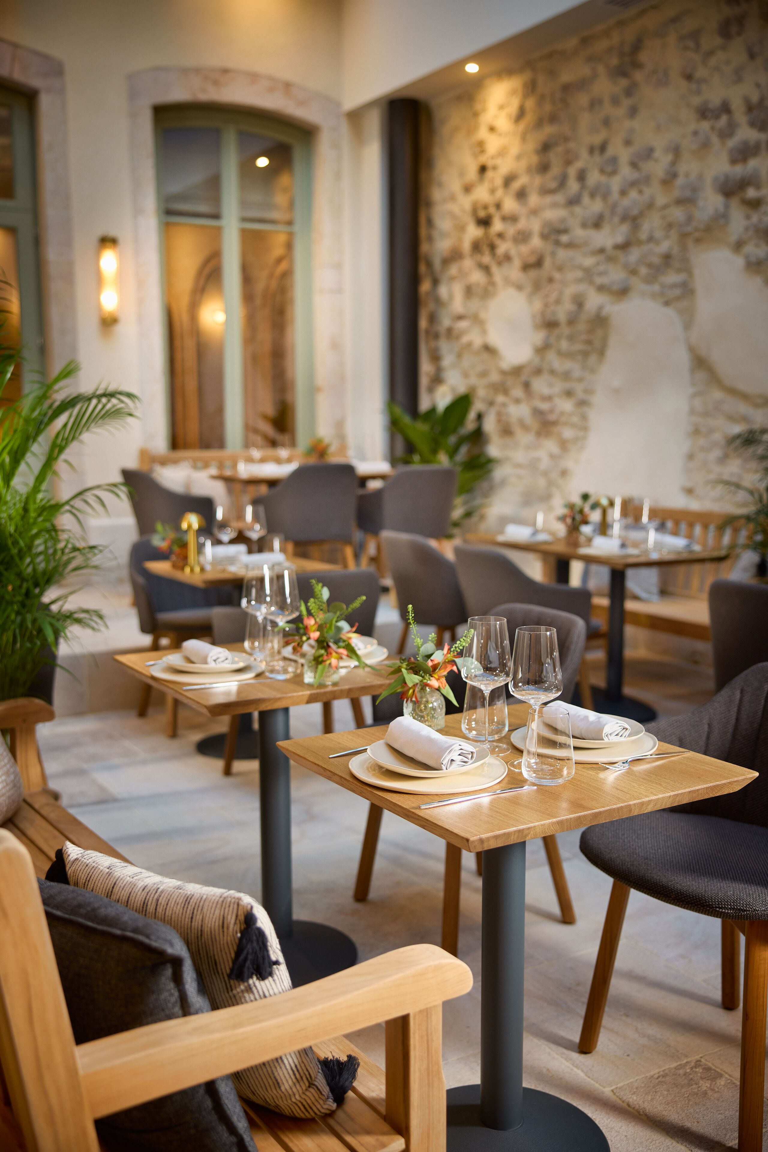 Un restaurante con mesas y sillas de madera, dispuesto con platos, vasos y flores.