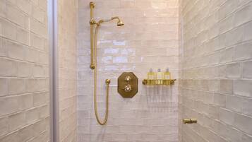 A walk-in shower with white tiled walls, a gold showerhead, and a handheld showerhead.