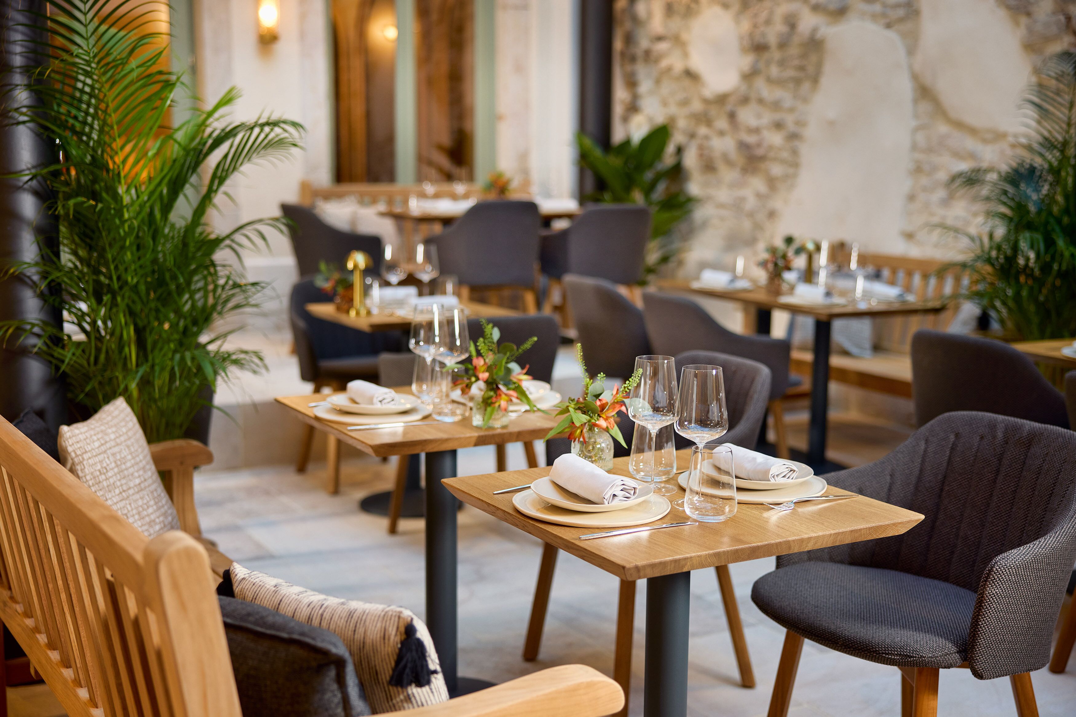 A restaurant interior with wooden tables and chairs, neatly set with plates, glasses, and cutlery.