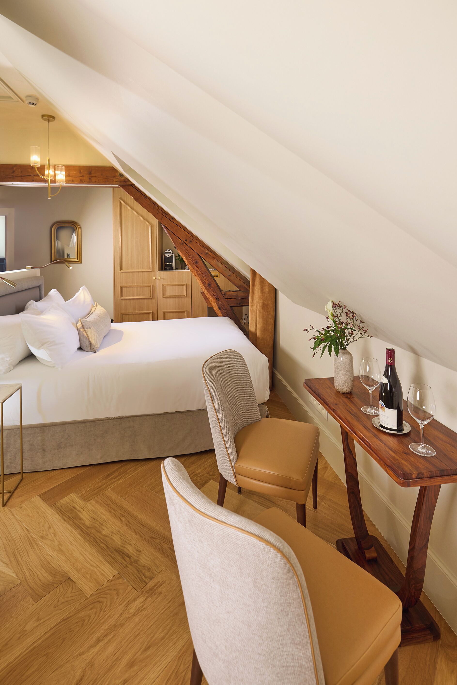 Een slaapkamer met een bed, een houten tafel met een vaas en wijnglazen, en een stoel.