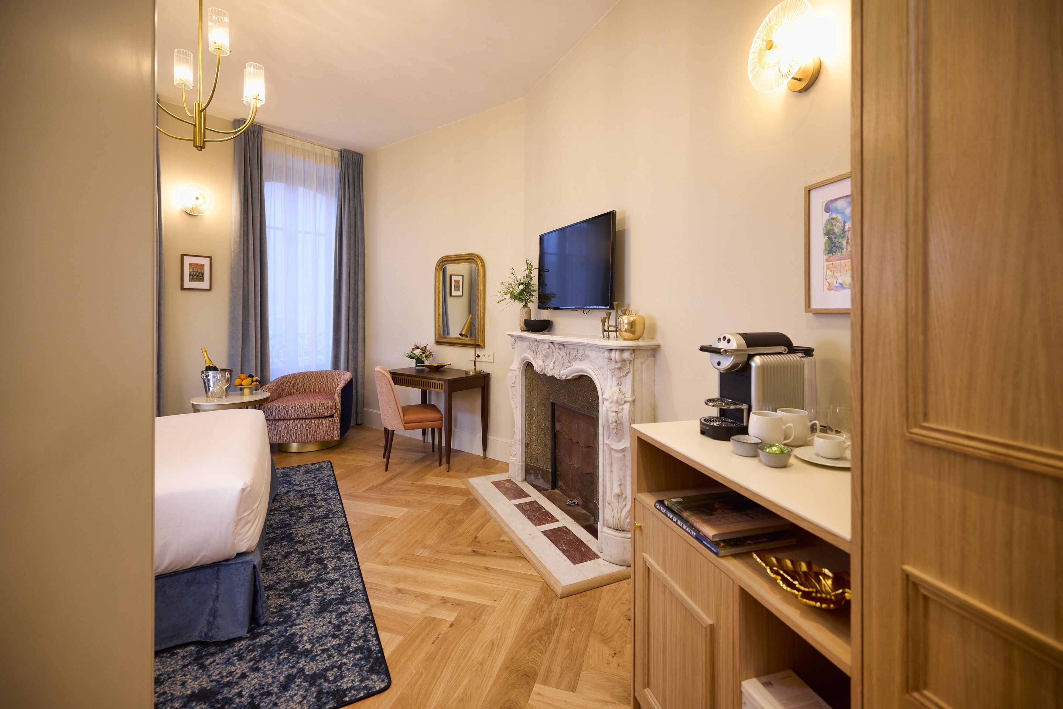 A hotel room with a bed, a sofa, a fireplace, a television, and a desk with a chair.