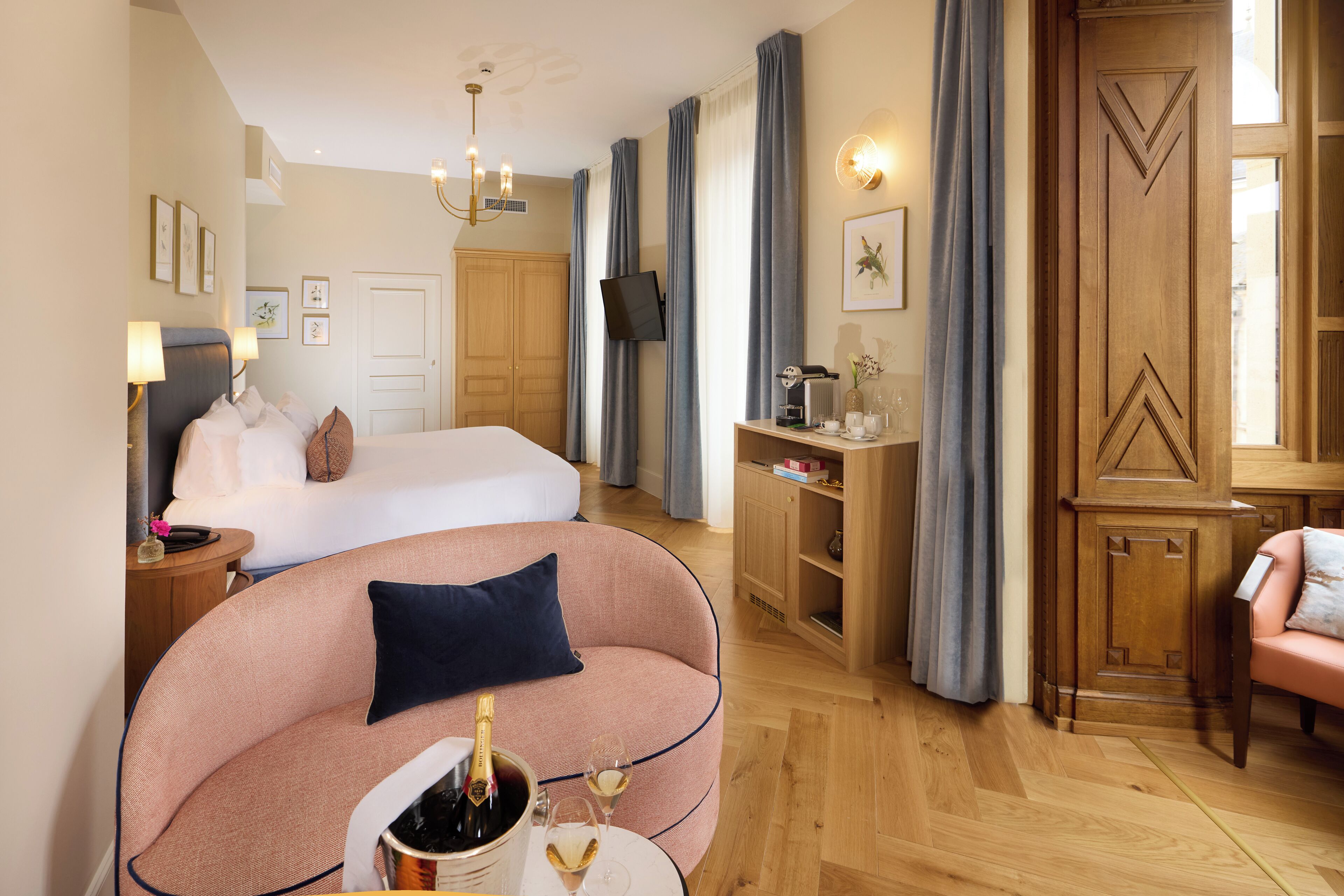 A hotel room with a bed, a sofa, a desk, a TV, and a minibar.