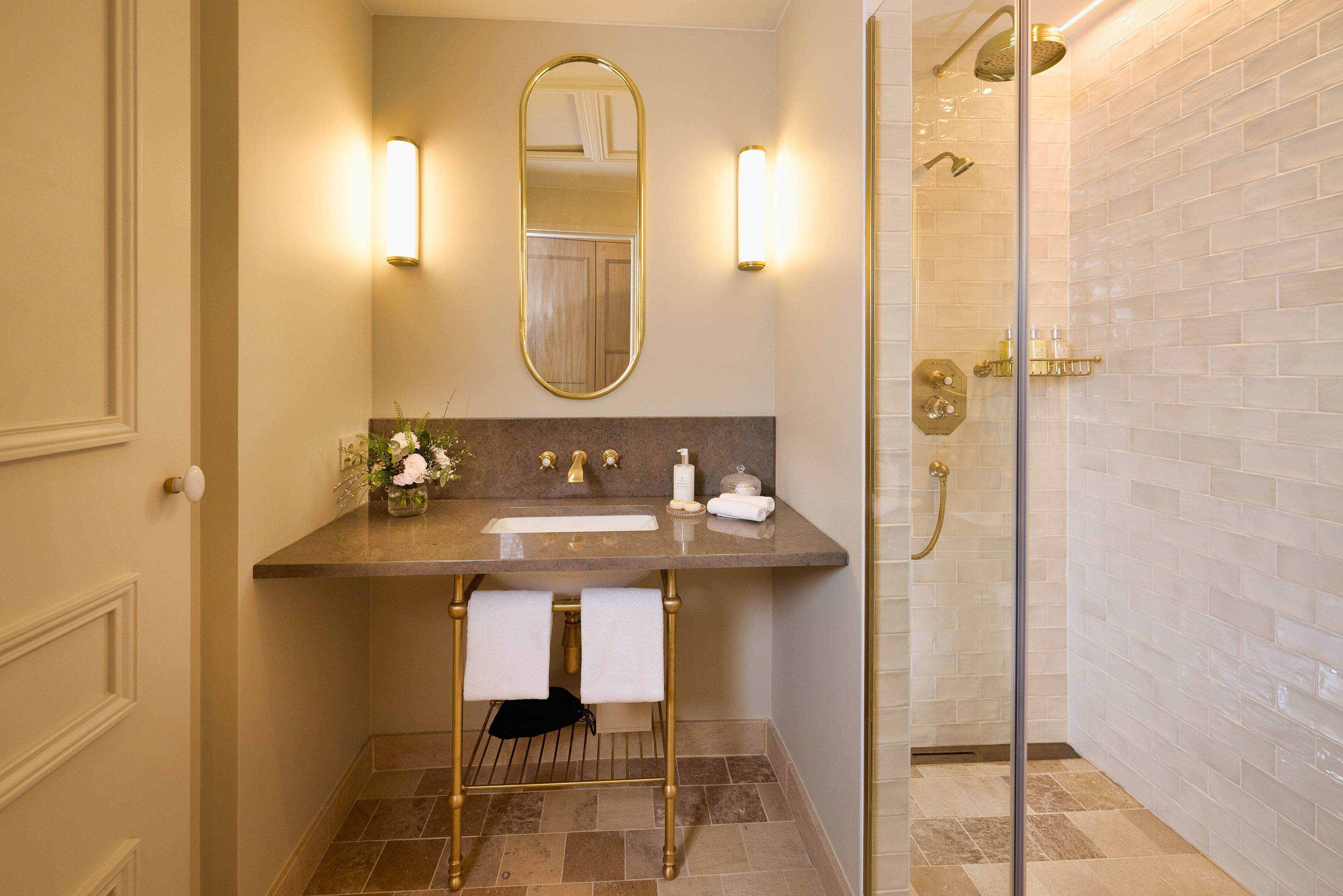 A bathroom with a vanity, mirror, towel rack, shower, and tiled walls.