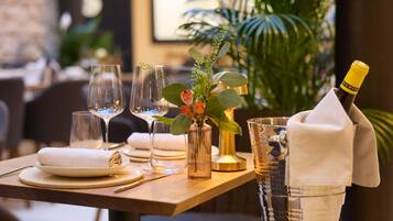 A well-set dining table with a bottle of champagne, a vase with flowers, and a glass pitcher.