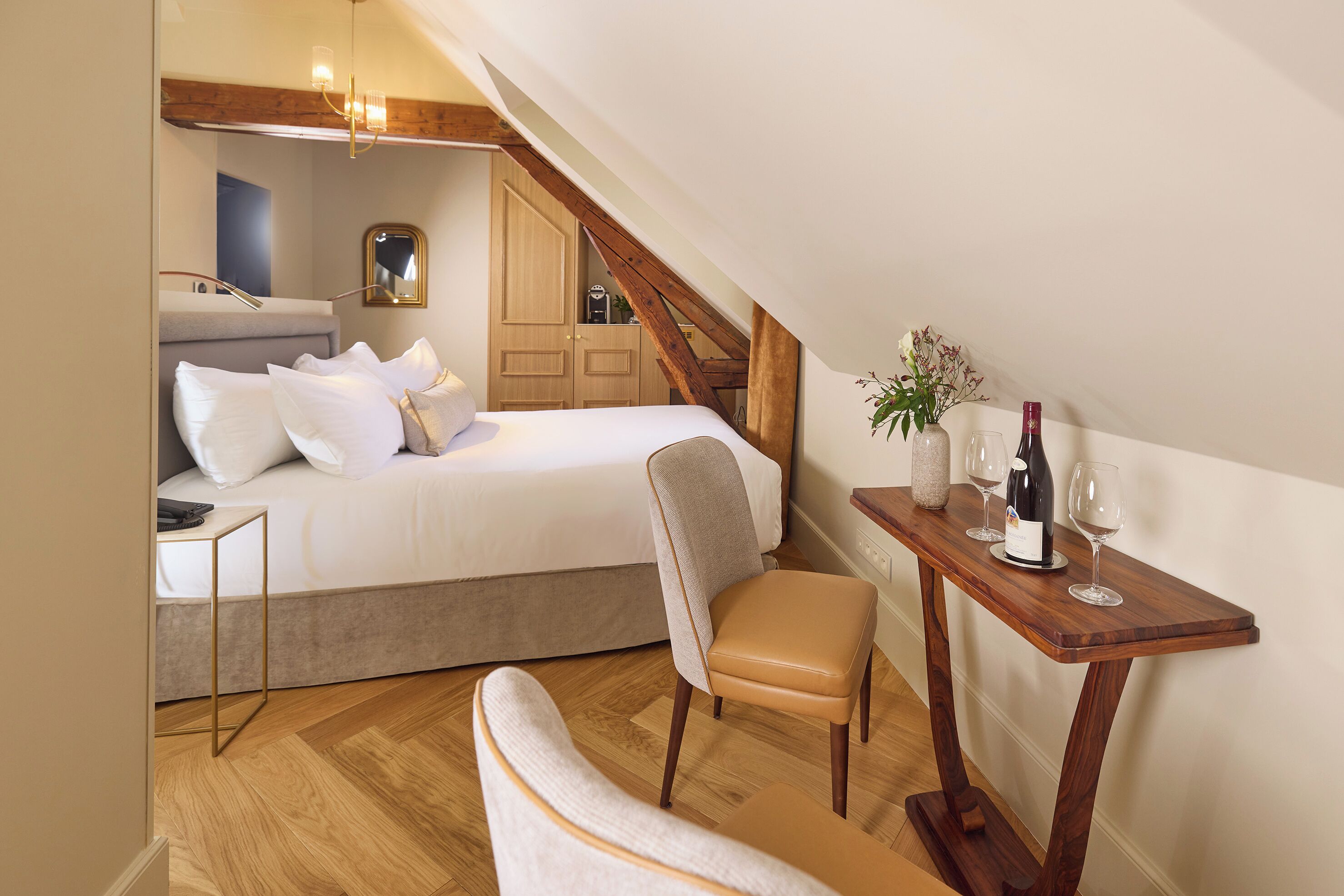 A bedroom with a bed, a chair, a table with wine glasses and a bottle, and a wooden staircase.