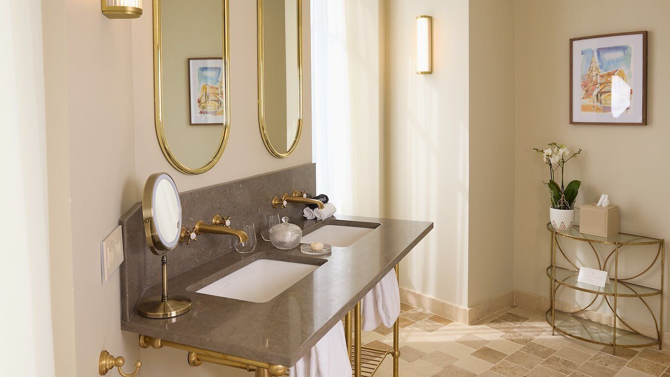 A bathroom with a marble vanity, gold fixtures, a large mirror, and a potted plant.