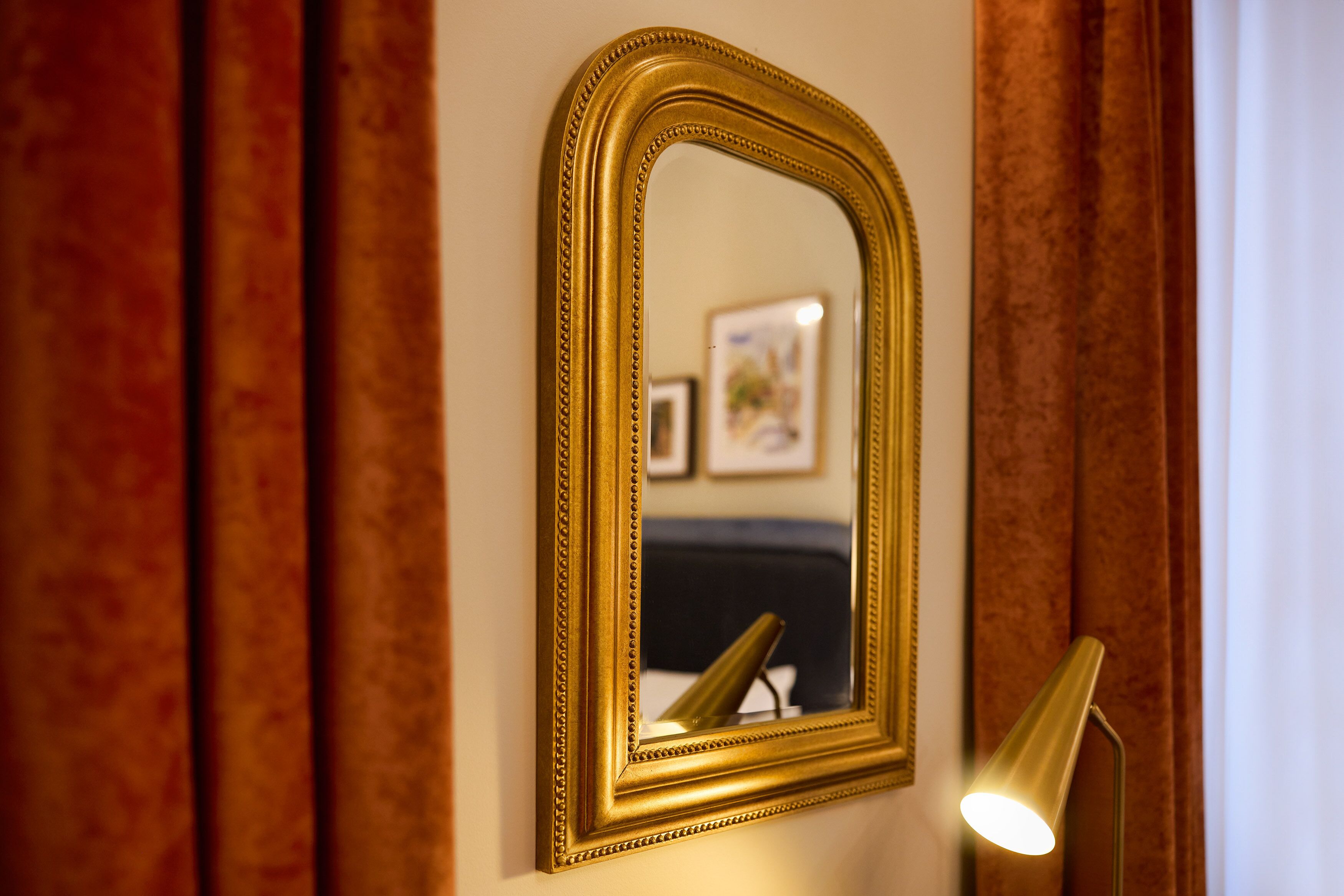 Espejo dorado en una pared con una lámpara a la derecha.
