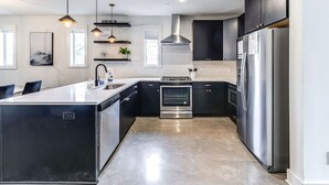 Una cocina moderna con una isla central, electrodomésticos de acero inoxidable, armarios negros e iluminación colgante.