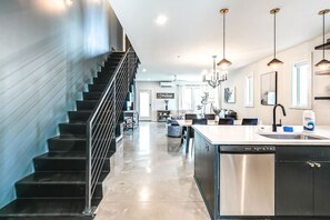 Une cuisine moderne dotée d’un îlot central, d’appareils électroménagers en acier inoxydable et de luminaires suspendus.