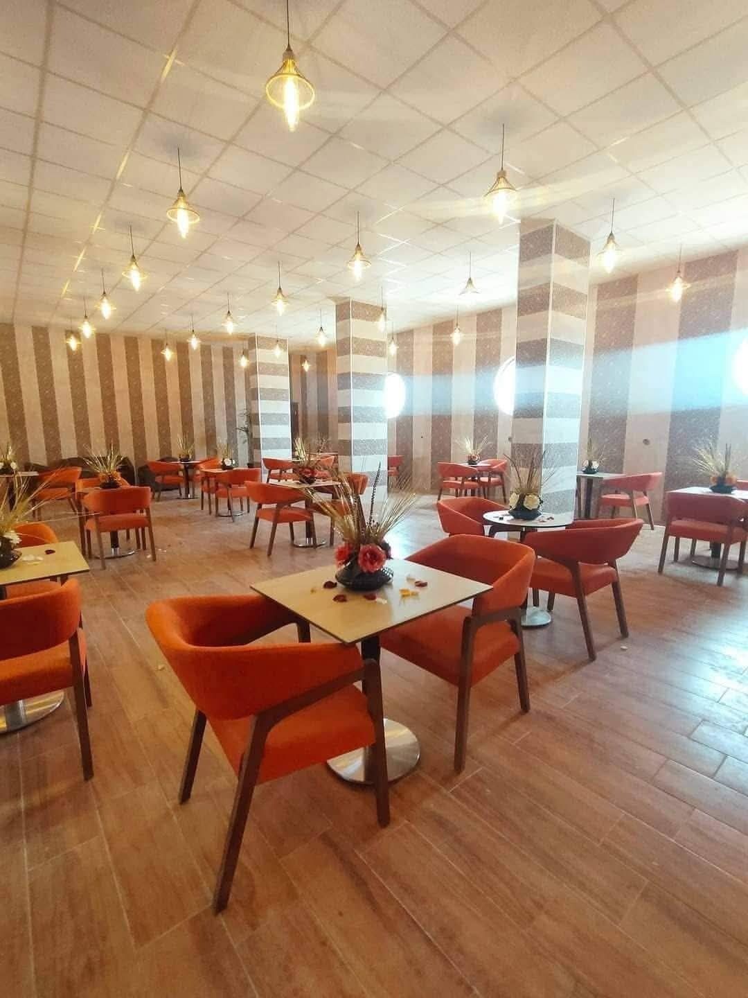 A spacious restaurant with high ceilings and modern pendant lighting. Tables are arranged in clusters, and the walls feature striped patterns.