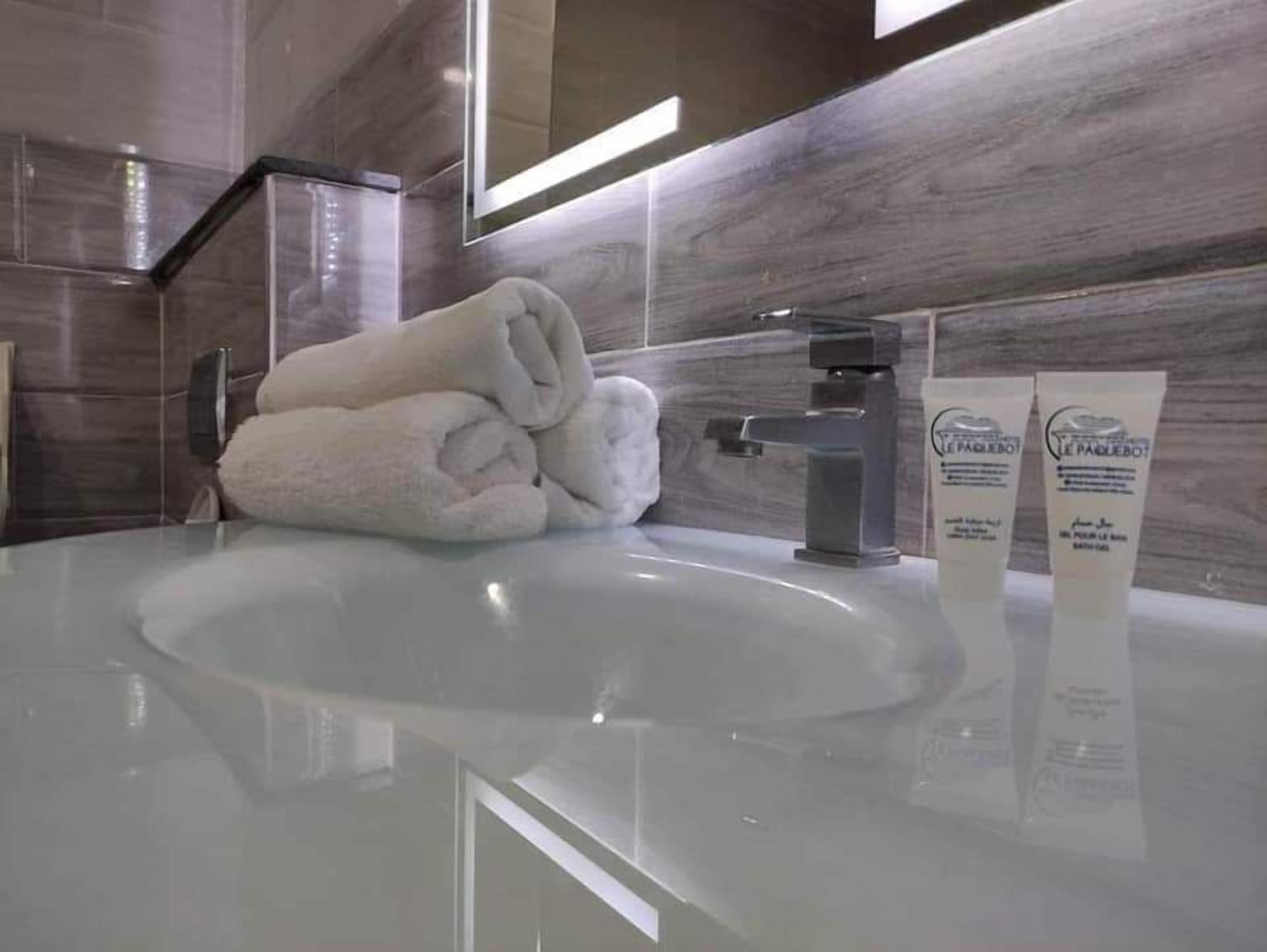 A modern bathroom with a large mirror, a white sink, and two bottles of lotion.